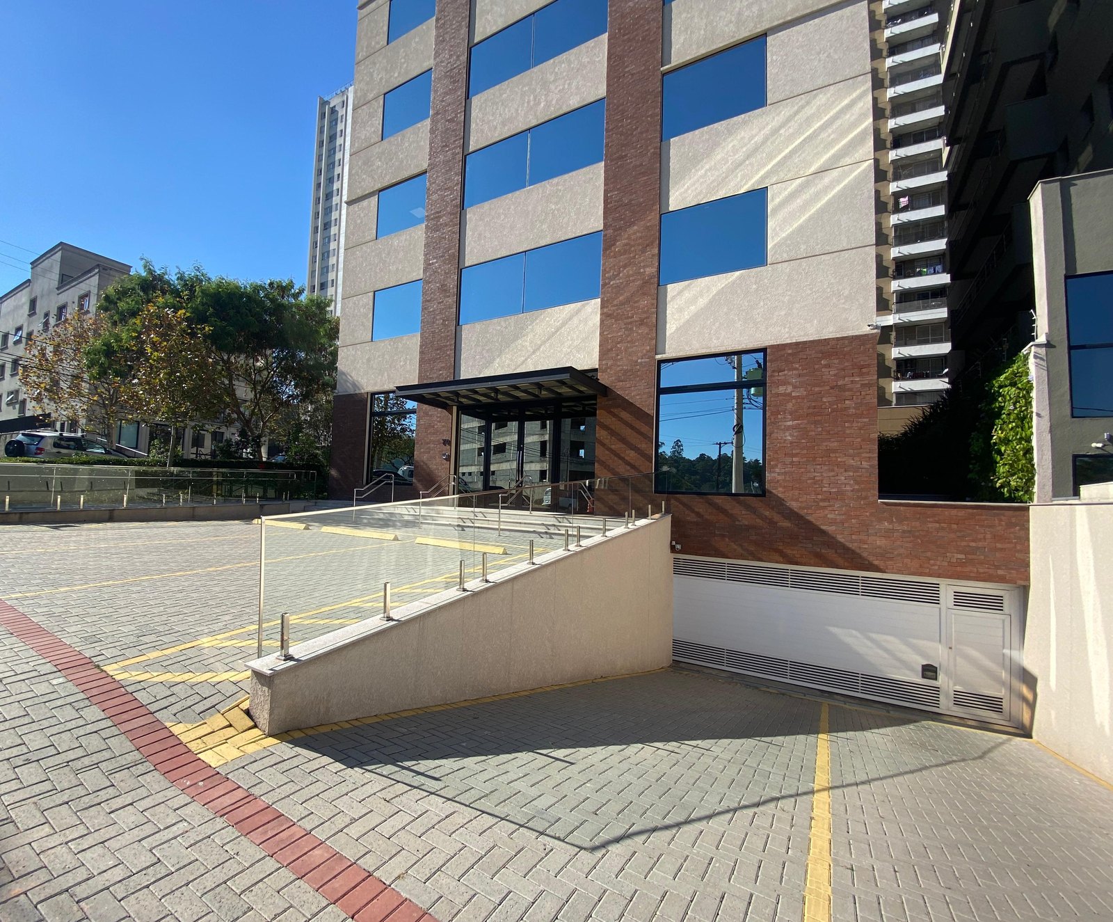 Entrada de prédio com vagas em piso intertravado, faixa vermelha e sinalização amarela